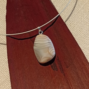 May include: A silver chain necklace with a white and brown agate pendant. The pendant is oval shaped and has a natural, organic look.