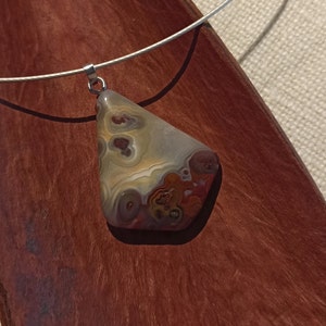 May include: A silver chain necklace with a pendant made of a brown, white, and red agate stone. The stone has a unique, swirling pattern.