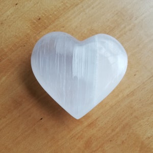 May include: A white heart-shaped selenite crystal on a wooden surface.