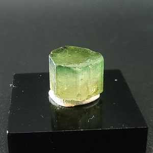 Peut inclure: Une pierre précieuse verte et jaune de forme hexagonale. La pierre précieuse est sur un présentoir noir.