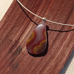 May include: A silver chain necklace with a teardrop-shaped pendant made of agate. The agate is a mix of red, white, and brown colors with a swirling pattern.