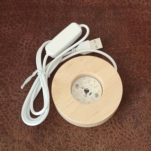 May include: A white USB-powered light base with a wooden circular platform and a white on/off switch. The light base has a circular array of small white LED lights.