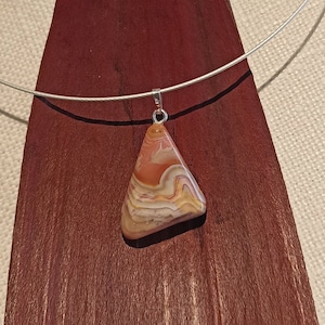 May include: A silver chain necklace with a pendant made of a triangular piece of agate with brown, orange, and white swirling patterns.