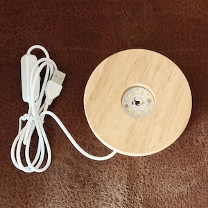 May include: A wooden base with a circular LED light in the center. The base is connected to a white USB cable with a switch.