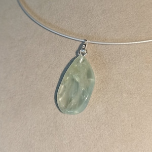 May include: A silver chain necklace with a light green gemstone pendant. The pendant is a smooth, oval-shaped stone.