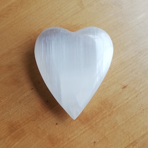 May include: A white selenite heart shaped crystal on a wooden surface.