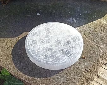 May include: A white selenite charging plate with a carved flower of life design. The plate is round and has a smooth, polished surface.