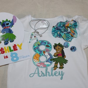 Puede incluir: Una camiseta blanca con un n&uacute;mero 8 bordado en azul y verde, un personaje de Stitch bordado en azul y verde, y el nombre "Ashley" bordado en azul. La camiseta forma parte de un conjunto de fiesta de cumplea&ntilde;os que incluye una coleta azul y verde, un collar azul y verde con un dije de la letra A, y un letrero redondo blanco con el texto "Ashley tiene 8 a&ntilde;os" y una caricatura de Stitch y Lilo.