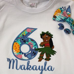 Puede incluir: Camiseta blanca con un n&uacute;mero seis bordado en azul, un personaje de dibujos animados y el nombre Makayla. El n&uacute;mero seis est&aacute; rodeado de un patr&oacute;n tropical colorido. Un lazo azul con un patr&oacute;n tropical est&aacute; en el hombro derecho de la camiseta.