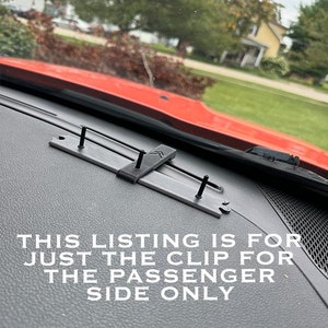 May include: A black plastic clip for a car sunshade. The clip is attached to the dashboard of a red car. The text "THIS LISTING IS FOR JUST THE CLIP FOR THE PASSENGER SIDE ONLY" is visible in the image.
