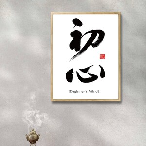 Pu&ograve; includere: Una stampa incorniciata con un design di calligrafia in bianco e nero dei caratteri giapponesi per "Beginner's Mind" in una cornice nera semplice su sfondo bianco. Il testo "[Beginner's Mind]" &egrave; stampato sotto la calligrafia.