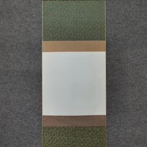 May include: A traditional Japanese scroll painting with a blank white center. The top and bottom sections feature a green floral pattern, separated by brown and tan bands. The scroll is suspended by a wooden bar and a metal hook.