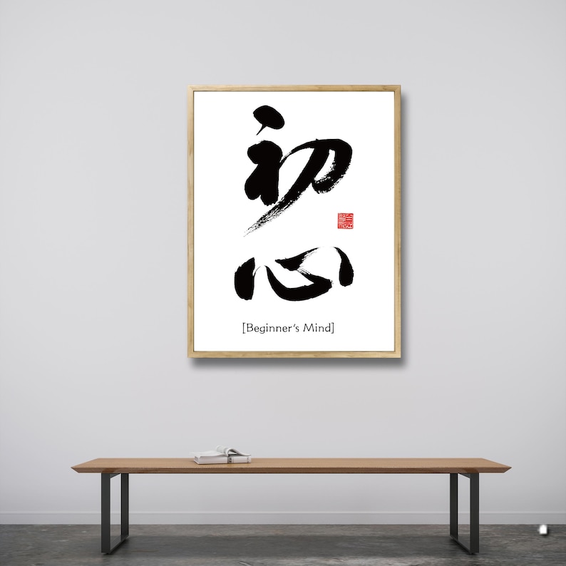 Pu&ograve; includere: Una stampa incorniciata con calligrafia nera su sfondo bianco. La calligrafia recita "Beginner's Mind" in inglese sotto i caratteri. La cornice &egrave; in legno chiaro.