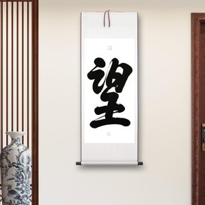 Puede incluir: Un rollo blanco con caligrafía negra en una pared blanca. La caligrafía es el carácter chino para "paz".