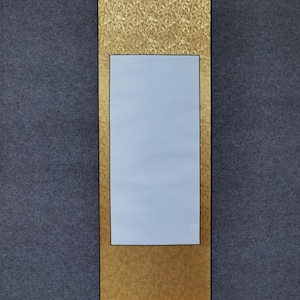 Puede incluir: Un rollo de pintura japonés tradicional con un borde de brocado dorado y un centro azul claro. El rollo tiene un rodillo negro en la parte inferior y herrajes decorativos en la parte superior.