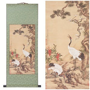 May include: A traditional Chinese scroll painting depicting two white cranes standing on a rocky outcropping. The cranes are surrounded by lush greenery, including a pine tree and flowering branches. The painting is done in a delicate style with muted colors.