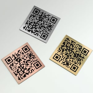 May include: Three square metal QR code plaques in silver, copper, and gold. Each plaque features a black QR code pattern. The plaques are arranged on a white surface.