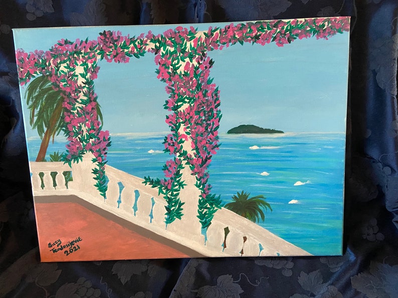 May include: A painting of a white balcony with a pink flower archway overlooking a blue ocean with a small island in the distance. The painting is signed "Suzy Taddei-Jones 2021".