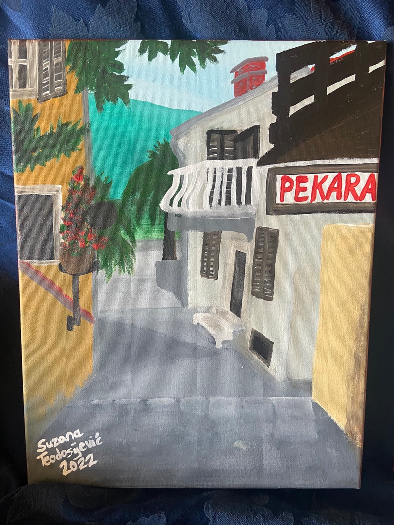 Puede incluir: Una pintura de una calle estrecha en un pueblo europeo. La calle est&aacute; bordeada de edificios, uno de los cuales tiene un letrero que dice "PEKARA." Los edificios est&aacute;n pintados en tonos de amarillo, blanco y marr&oacute;n. Hay &aacute;rboles y plantas en primer plano. La pintura est&aacute; firmada "Suzana Teodosjevic 2022."