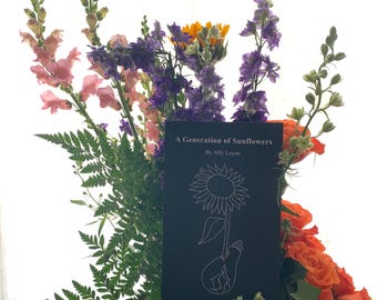 Può includere: Un libro nero intitolato "A Generation of Sunflowers" di Ally Loyns. Il libro è circondato da un bouquet di fiori, tra cui bocche di leone viola, rose arancioni e felci verdi.