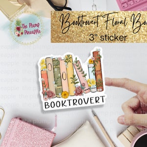 May include: A 3-inch sticker featuring a stack of colorful books with floral accents. The sticker says "Booktrovert" in white text on a white background.