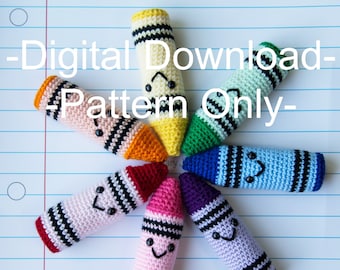 May include: A set of seven crocheted crayon toys with smiling faces. The crayons are arranged in a circle on a white and blue lined paper background. The crayons are yellow, green, blue, purple, pink, red, and orange.