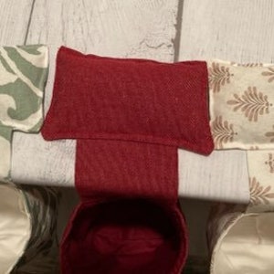 May include: Three fabric-covered heat packs, one red, one green, and one with a brown floral pattern. Each pack is sitting on a white surface.