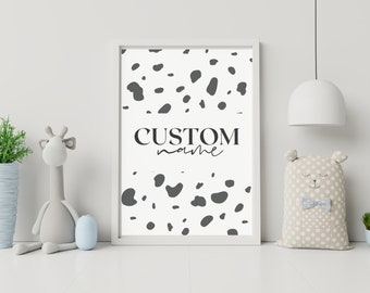 Peut inclure: Une affiche encadrée avec un fond blanc et un motif de taches grises foncées. Le texte "CUSTOM name" est centré sur l'affiche. Une girafe en peluche, un oreiller en forme d'ours et des plantes en pot sont au premier plan.