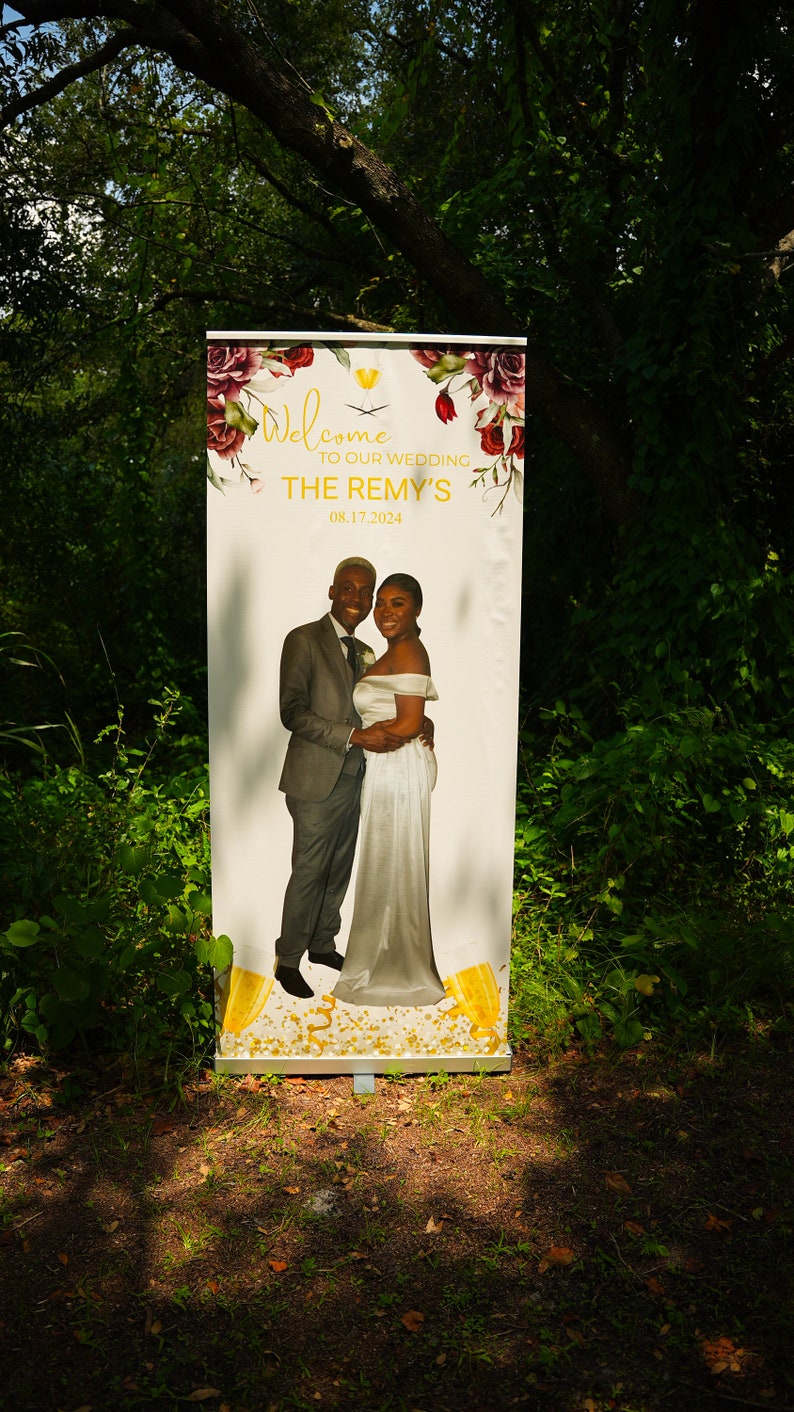 May include: A white wedding sign with floral designs and a photo of a couple. The sign reads "Welcome to our wedding The Remy's 08.17.2024".