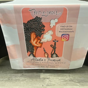 May include: A pink and white table cover with a cartoon illustration of a woman smoking a hookah. The text on the table cover reads "Bust-A-Smoke, LLC", "Find us on Instagram #bustasmokellc", "Atlanta's Premium Hookah Catering Service", "bustasmokeati@gmail.com", and "470-781-2202".