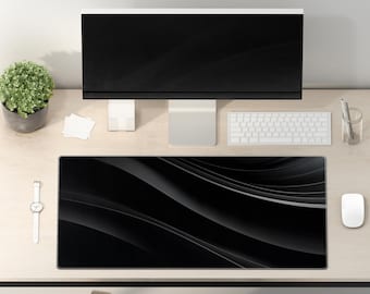 Puede incluir: Una alfombrilla de escritorio negra con un diseño de ondas sutil. La alfombrilla está sobre un escritorio de madera clara con un monitor de ordenador, un teclado, un ratón y una planta en maceta.