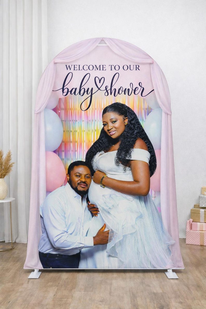 Puede incluir: Un tel&oacute;n de fondo de baby shower con una pareja. El tel&oacute;n de fondo tiene un arco rosa con las palabras "WELCOME TO OUR baby shower" en escritura. Se ven globos rosas y azules. La mujer lleva un vestido blanco y el hombre una camisa azul claro.