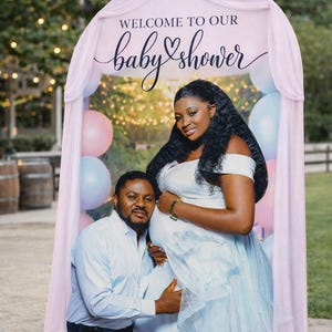Puede incluir: Un tel&oacute;n de fondo de baby shower con una pareja. El tel&oacute;n de fondo tiene el texto "WELCOME TO OUR baby shower" en escritura. La mujer lleva un vestido azul claro y el hombre una camisa azul claro. Se ven globos rosas y azules.
