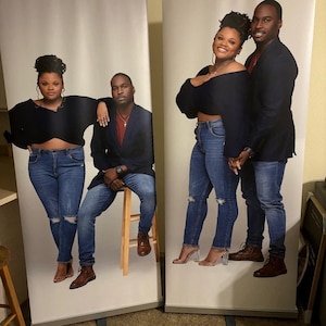 May include: Two couples pose for a photo in front of a white backdrop. The women are wearing black tops and blue jeans. The men are wearing suits and blue jeans.