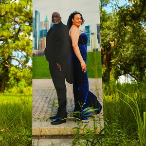 May include: A black and white photo of a couple standing in front of a city skyline. The man is wearing a black suit and the woman is wearing a blue dress. The photo is printed on a banner.