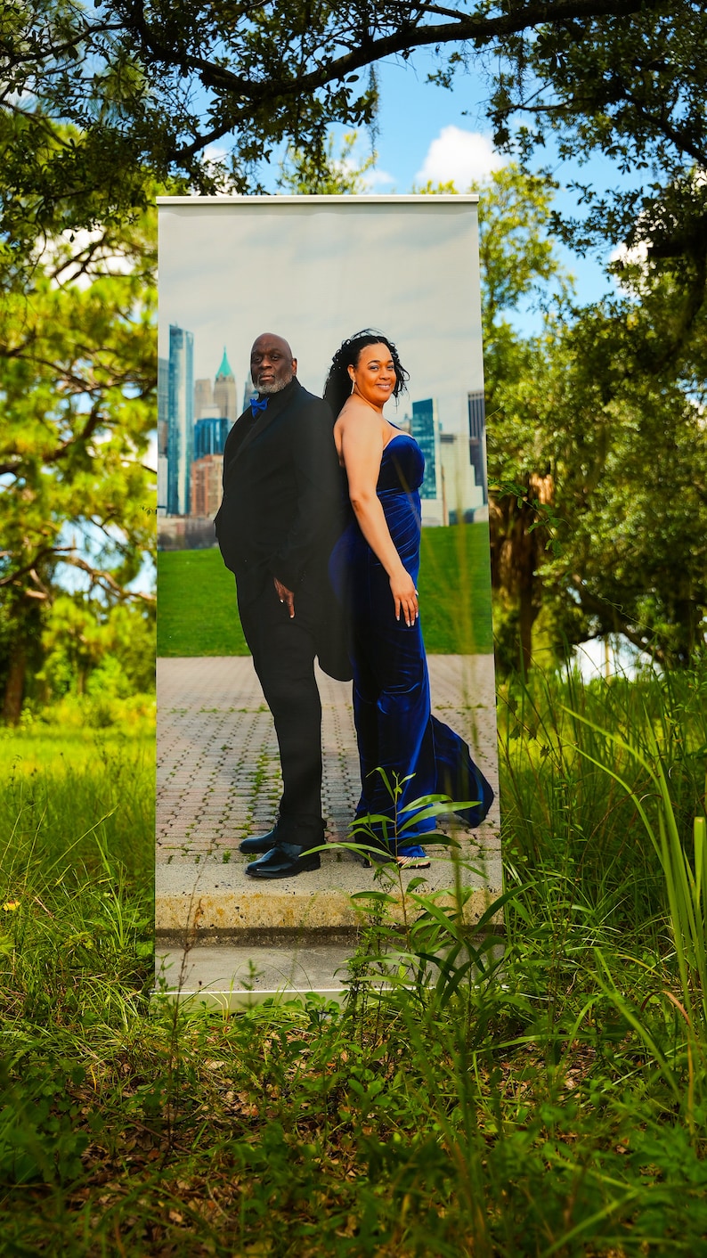 May include: A black and white photo of a couple standing in front of a city skyline. The man is wearing a black suit and the woman is wearing a blue dress. The photo is printed on a banner.