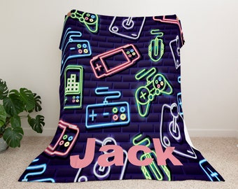 May include: A soft, blue fleece blanket with a neon-colored pattern of video game controllers, joysticks, and a mouse. The blanket has the name "Jack" printed in pink on the bottom.