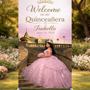 Può includere: Un grande cartello rettangolare con la scritta dorata "Welcome to my Quinceañera Isabella June 14, 2026". Il cartello presenta una foto di una giovane donna in abito rosa e tiara. Lo sfondo è un ambiente esterno panoramico.