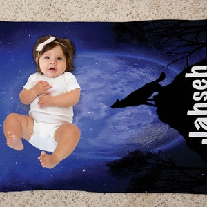 Puede incluir: Una manta para beb&eacute; azul y negra con un lobo blanco aullando a la luna. La manta tiene un fondo de cielo nocturno estrellado y el nombre "Jahseh" impreso en blanco en el lado derecho.