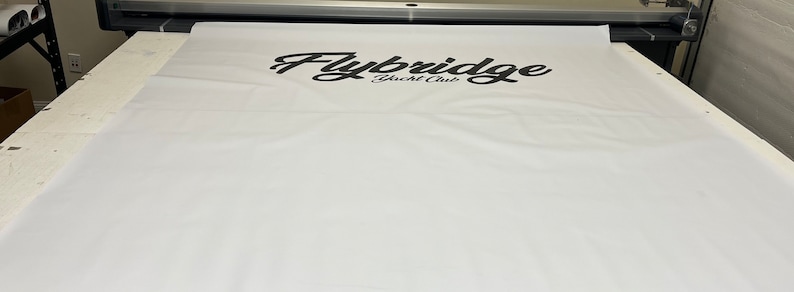 Pu&ograve; includere: Uno striscione bianco con il testo "Flybridge Yacht Club" stampato in nero.