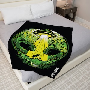 May include: Black fleece blanket with a green and yellow graphic of a UFO over a forest. The text "MEGAN" is printed on the bottom right corner of the blanket.