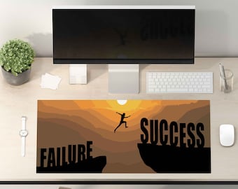May include: A motivational desk mat featuring a silhouette of a person leaping from a cliff labelled "failure" to a cliff labelled "success". The background is a sunset with orange and brown tones.