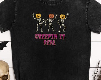 May include: Black t-shirt featuring a Halloween design. The graphic includes three dancing skeleton figures with pumpkin heads, and the text "CREEPIN IT REAL" in pink and purple. The shirt has a slightly faded, vintage look.