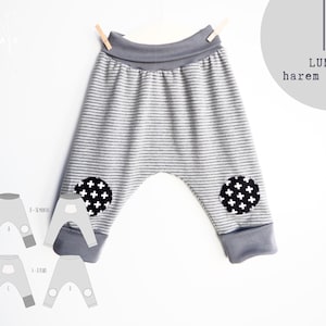 Può includere: Pantaloni harem a righe grigie e bianche con toppe a croce bianche e nere sulle ginocchia. I pantaloni hanno un girovita e polsini grigi. Il testo "LUNA harem pants" è visibile.