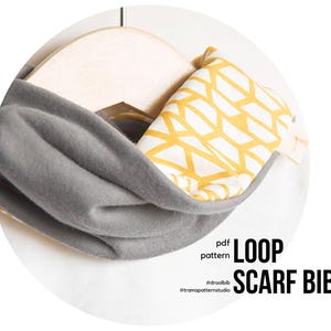 Puede incluir: Un babero con bufanda de bucle gris con un patrón geométrico amarillo y blanco en el interior. La bufanda está doblada y colocada sobre una percha de madera. El texto en la imagen dice "LOOP SCARF BIB" y "pdf pattern".