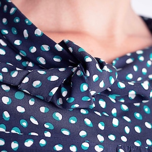May include: Close-up of a navy blue fabric with a white and teal polka dot pattern. The fabric is gathered at the neckline and forms a bow. The image focuses on the details of the fabric and its design.
