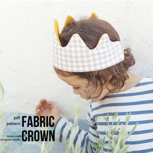 Puede incluir: Un niño que lleva una camisa a rayas azules y blancas lleva una corona de tela de gingham gris y blanca con ribete amarillo. La corona tiene una parte superior puntiaguda y tiene forma de corona. El niño está mirando hacia abajo a algo fuera de cámara. El texto "pdf pattern FABRIC CROWN #playcrown #tromapatternstudio" es visible en la imagen.