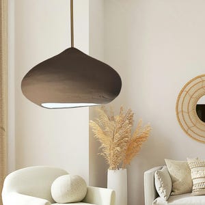 Könnte beinhalten: Eine dunkelbraune Pendelleuchte in organischer Form mit glatter, matter Oberfläche. Die Lampe besteht aus einem breiten, abgerundeten Kuppelkörper, der an einer dünnen, geraden Metallstange hängt, mit einer weißen Lichtöffnung an der Unterseite.