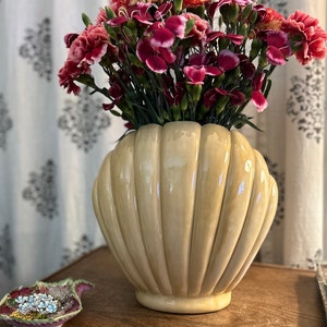 May include: A bouquet of pink and burgundy carnations in a cream-colored ceramic vase shaped like a seashell.