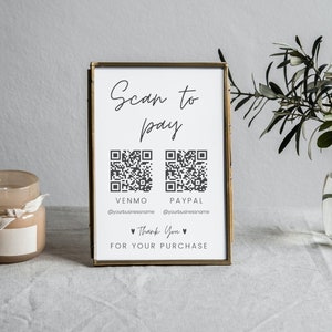 May include: A gold framed sign with the text "Scan to Pay" and two QR codes labeled "Venmo" and "Paypal". The sign also includes the text "@yourbusinessname" and "Thank You for your purchase".